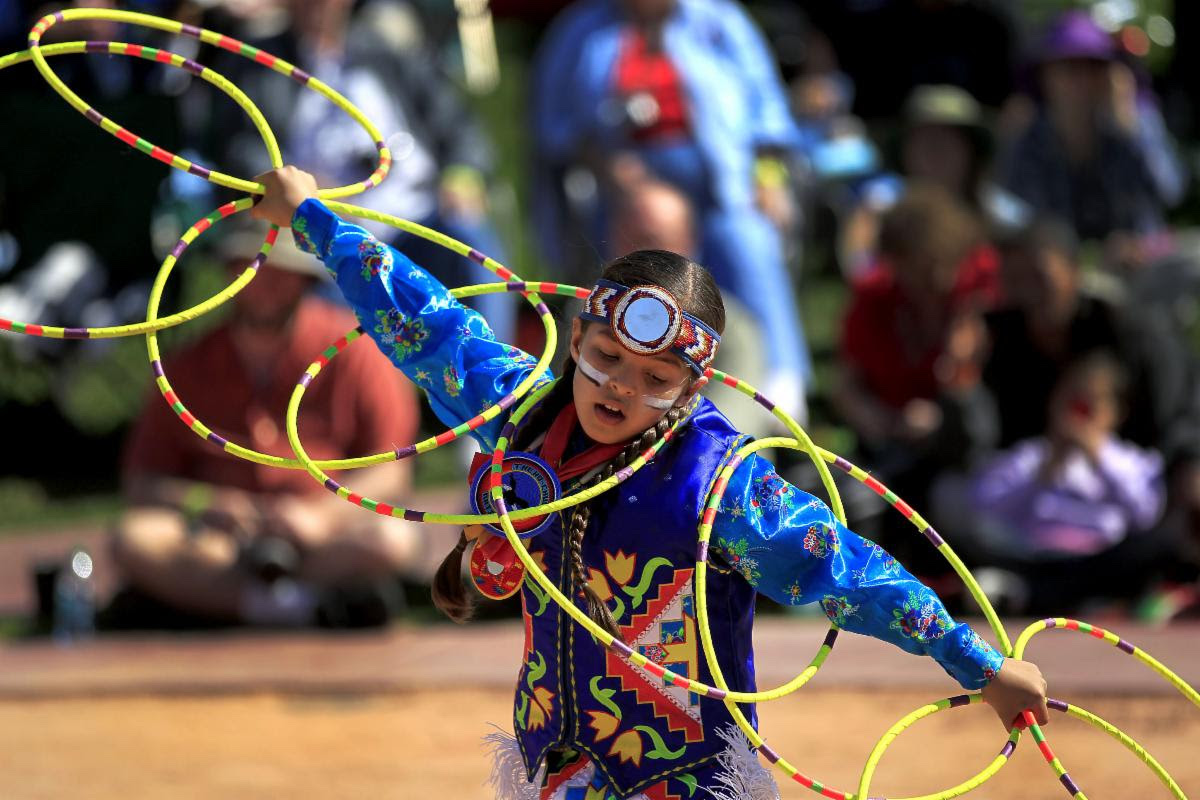 A young kid wearing a colorful indian outfit dancing outside.